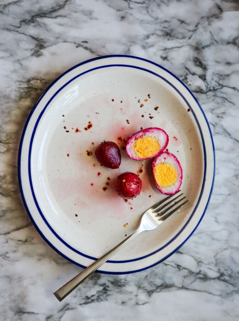 Pickled eggs cut in half with a beet and a fork on a plate